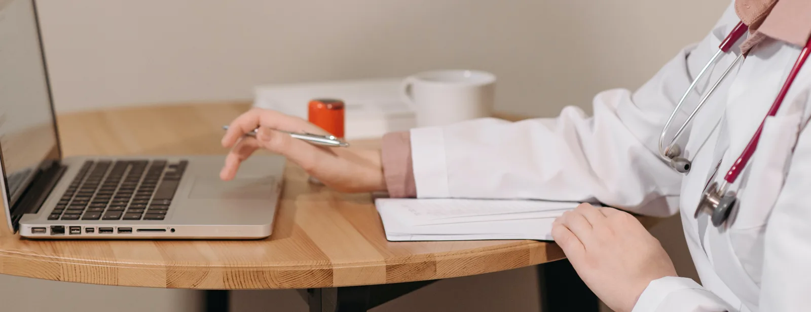 A clinician working at a laptop across the table from a patient
